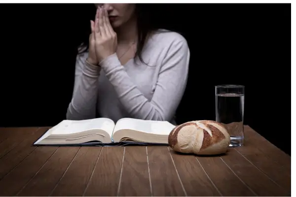 Pessoa jejuando com a Bíblia aberta e um pão sobre a mesa, representando o momento de consagração e reflexão sobre como fazer jejum para Deus.